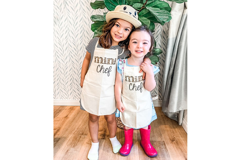 These two girls wear aprons printed with the words Mini Chef, made by Wendy and Wander on its Roland DG VersaStudio BT-12 DTG printer.